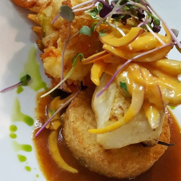 Peruvian dish with fried seafood, yellow sauce, microgreens, and a green drizzle on a white plate.