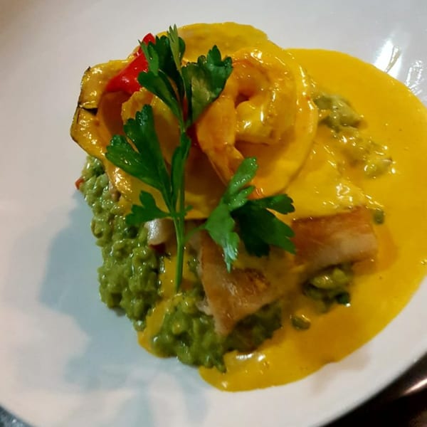 Peruvian dish with yellow sauce, green rice, fish, red pepper, and parsley on a white plate.