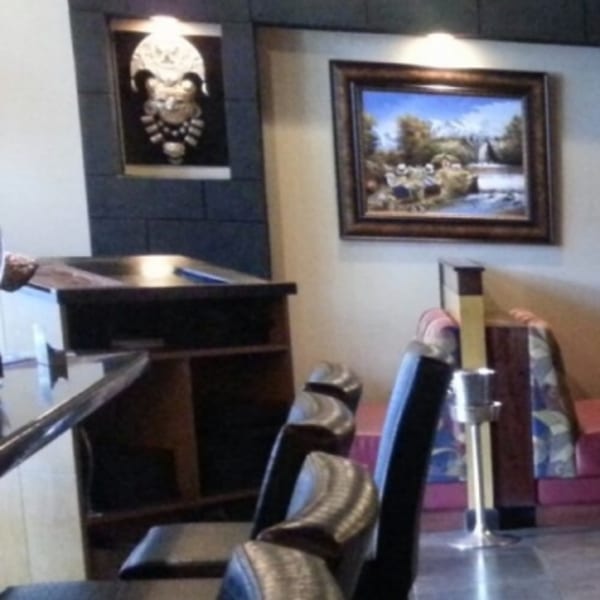 Restaurant interior with Peruvian art, a landscape painting, and dark wooden furniture with chairs.