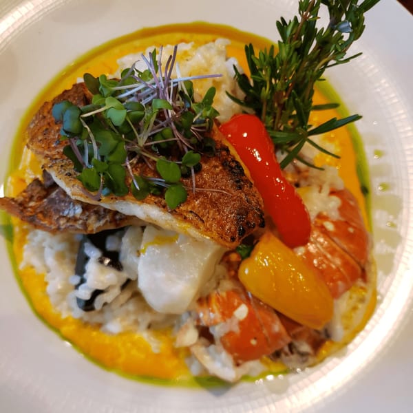 Peruvian seafood dish with crispy fish, rice, lobster, peppers, and herbs on a white plate.