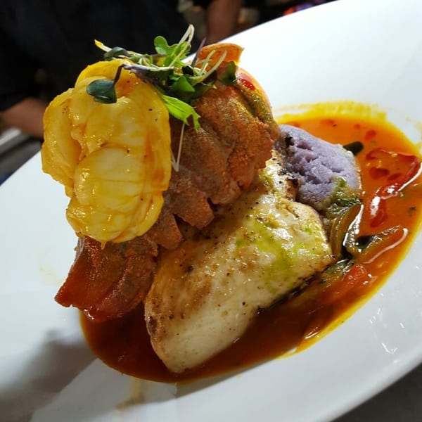 Peruvian seafood dish with shrimp, fish, purple mashed potatoes, and red sauce on a white plate.