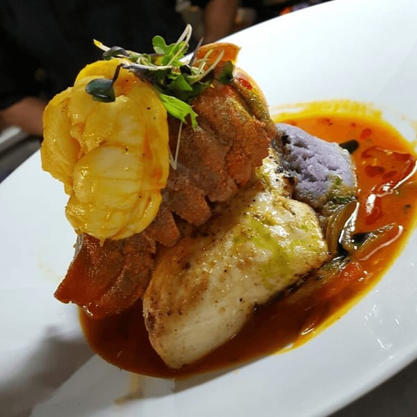 Peruvian seafood dish with shrimp, fish, purple mashed potatoes, and red sauce on a white plate.