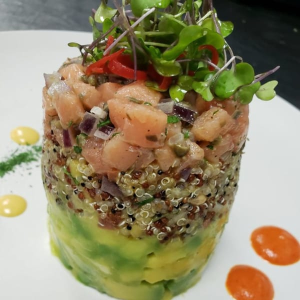 Peruvian salmon tartare with avocado, quinoa, and microgreens, garnished with red pepper and sauces.