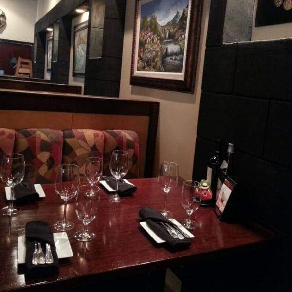 A Peruvian restaurant dining room with a set table, patterned booth seating, and framed artwork.