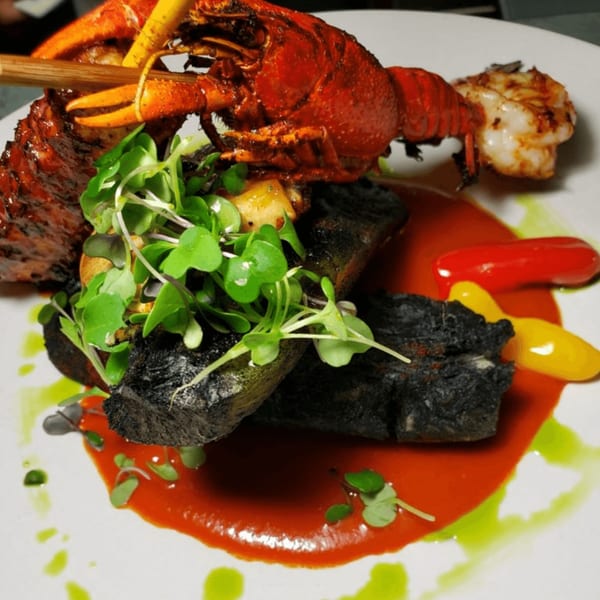 Peruvian dish with grilled lobster, dark-crusted meat, microgreens, and red and green sauces.