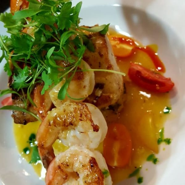 Peruvian grilled shrimp and fish with fresh herbs, tomatoes, and a vibrant yellow sauce.