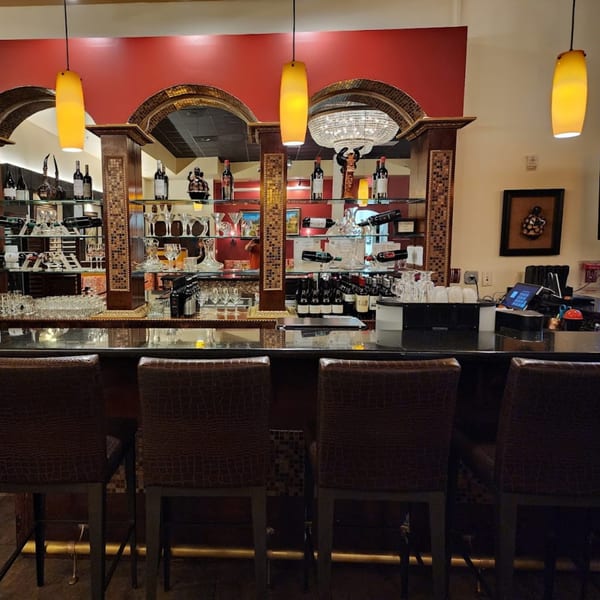 El Chaman Peruvian Cuisine bar with bottles, glasses, and four bar stools.