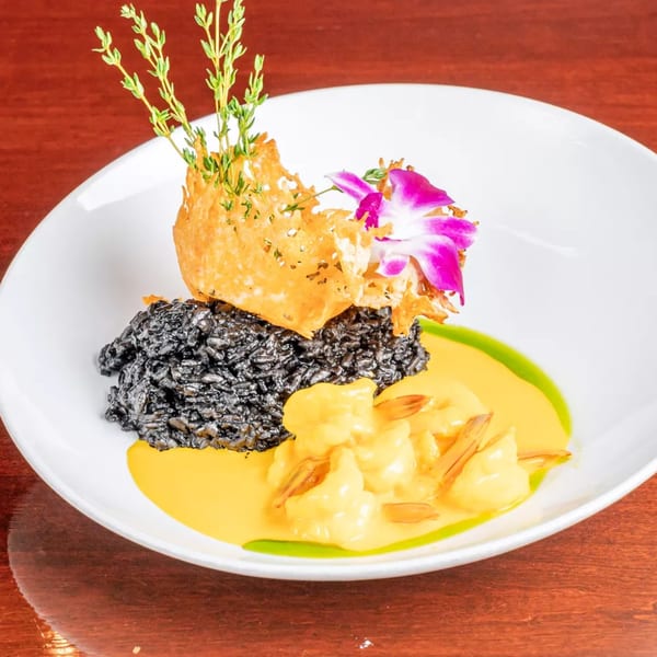 Gourmet plate featuring black rice, creamy shrimp, crispy garnish, fresh herbs, and purple edible flowers.