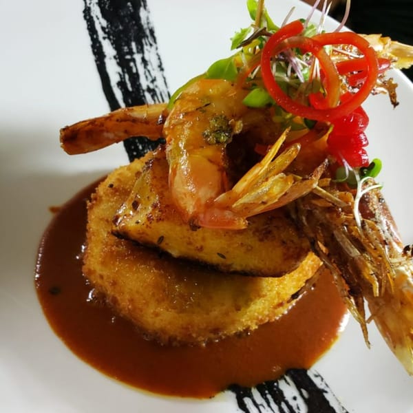 Peruvian dish with crispy fried shrimp, a golden-brown potato cake, and rich brown sauce.