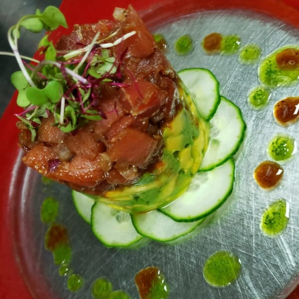 Peruvian tuna tartare with avocado, cucumber slices, and microgreens on a clear plate.